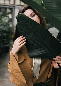 woman in brown long-sleeve blouse behind green leaf during daytime thumbnail