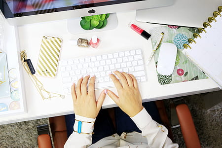 person in white long-sleeved top using wireless keyboard on white wooden table thumbnail