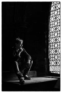 grayscale photography of man sitting on stairs near window thumbnail