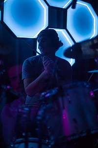 man holding drum stick playing drum near the black and blue wall thumbnail