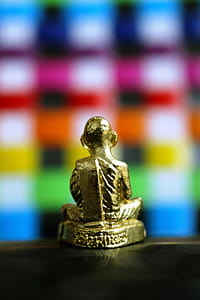 Back view of a golden Buddha statue isolated against a bright multi colored checked background thumbnail