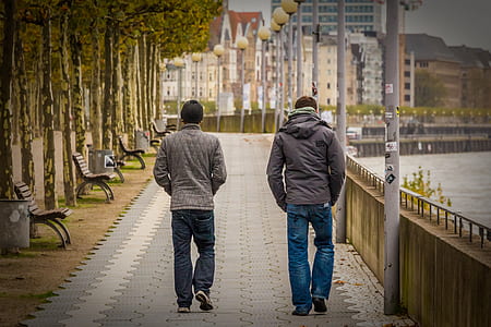 two men walking near body of water during daytime thumbnail