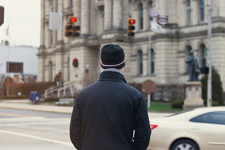 man in black jacket and black hat standing near beige sedan at daytime thumbnail