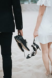man and woman carrying footwear walking on brown sand thumbnail