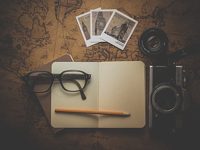 eyeglasses, pencil, planner, camera, and photos on brown map thumbnail