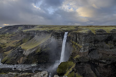 green and brown water falls under cloudy sky thumbnail