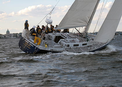 blue and white sailboat tipping to one side while group of people are standing on the other side thumbnail