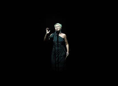 woman wearing black one-shoulder dress standing in front of microphone stand thumbnail