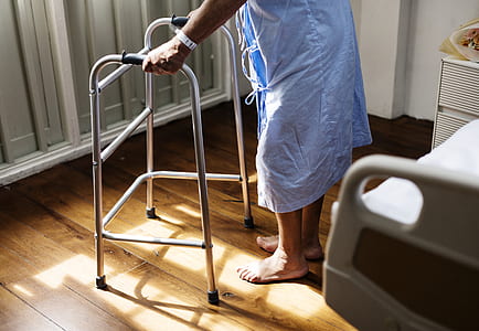 Person in Hospital Gown Using Walking Frame Beside Hospital Bed thumbnail