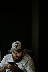 man in gray T-shirt sitting on chair while using smartphone thumbnail