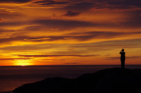 silhouette photo of person standing on cliff near body of water thumbnail