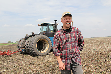 man in plaid sport shirt standing near tractor thumbnail