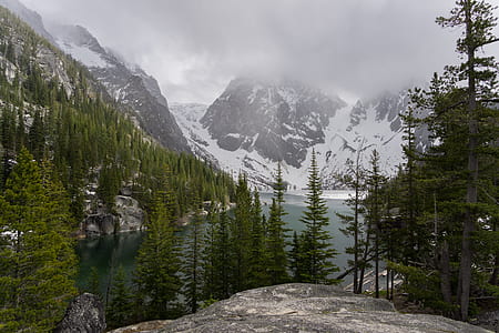 clouds covering peak of mountain near body of water and trees thumbnail