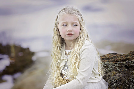 girl in white cardigan sitting on stone during daytime thumbnail