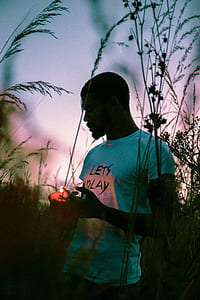 man in teal shirt holding lighter surrounded with plants during sunset thumbnail
