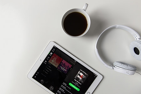 Headphones, coffee and iPad tablet with Spotify music app open on a white desk thumbnail