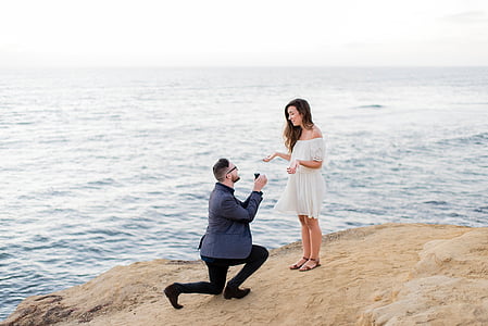 men proposing in front of woman on cliff near body of water at daytime thumbnail