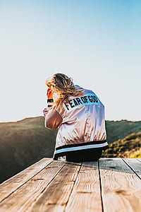 woman sitting on brown deck wearing gold and black Fear of God-printed jacket thumbnail
