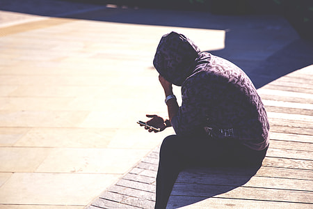 A man wearing a hoodie checks his mobile iPhone smartphone in an urban setting thumbnail