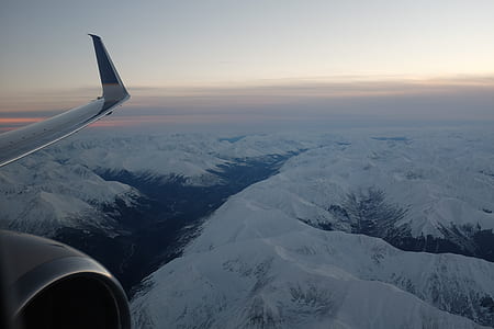 airliner flying over mountain range covered in snow during daytime thumbnail