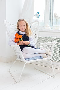 girl holds orange rose flowers while sitting on white metal armchair thumbnail