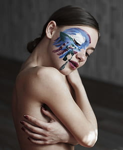 selective focus photography of woman with paint on face hugs herself thumbnail