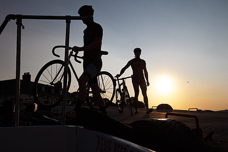 silhouette photo of two men holding bicycles thumbnail