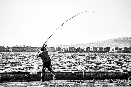 Grayscale Photography of Man Holding a Fishing Rod Near Body of Water thumbnail