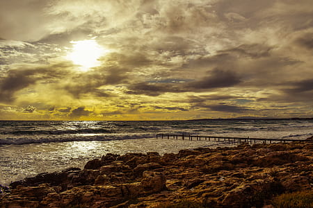 gray dock near rocky seashore during golden hour thumbnail