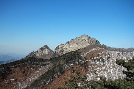 low angle photo of rocky tree covered hill under blue skies thumbnail