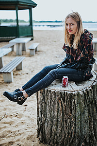 Beautiful blonde woman relaxing with a can of coke on a tree stump by the beach thumbnail