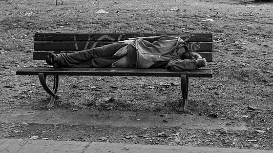 grayscale photography of man wearing jacket sleeping on wooden bench thumbnail