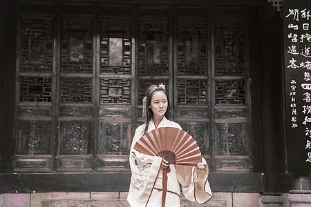 woman wearing white dress holding red fan near black wall thumbnail