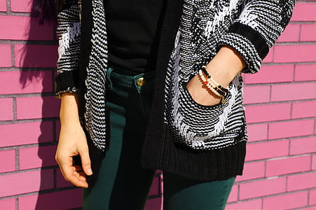 woman wearing grey and black cardigan leaning on pink brick wall thumbnail