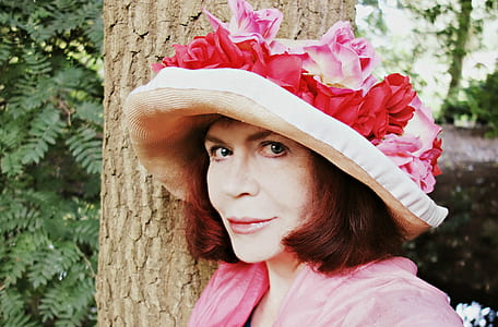 woman in pink top and hat leaning on tree outdoors thumbnail