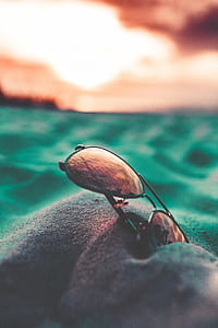 selective focus photography of brown lens Aviator-style sunglasses with black frames in sand under orange sky thumbnail
