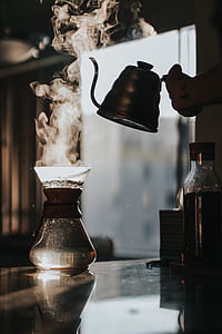 person holding kettle above clear glass container thumbnail