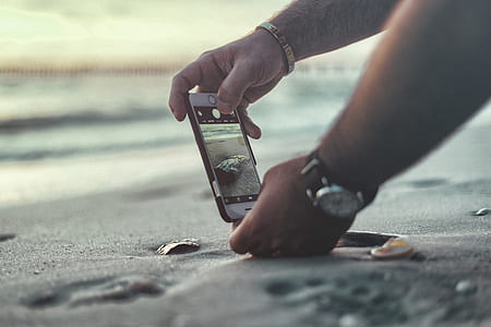 person holding silver iPhone with black case taking photo of black stone thumbnail