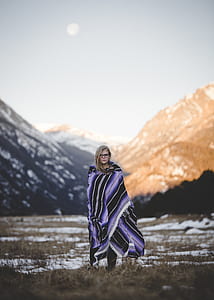 woman standing on snow-covered barren field across mountain range photo during daytime thumbnail