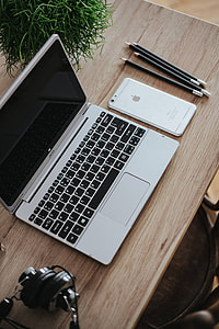 Silver Acer laptop on a wooden desk with a green plant, pencils and an Apple iPhone thumbnail