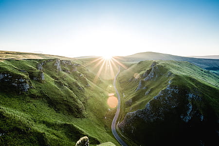 landscape photo of road in middle of mountains leading to sun thumbnail