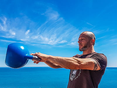 Man Wearing Black Shirt Holding Kettle Bell Near Body of Water thumbnail