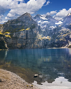 selective focus photo of mountain near body of water under white clouds and blue sky thumbnail