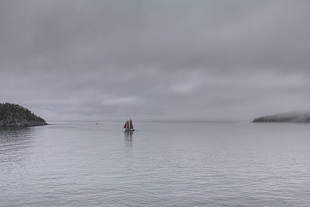 red sailboat on water under gray clouds thumbnail