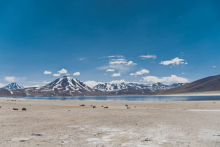 person taking photo of blue body of water near snow covered mountains at daytime thumbnail