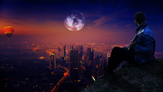 man sitting on hill while playing guitar under dark sky thumbnail