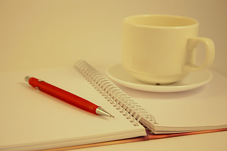 white ceramic teacup on saucer on top of opened notebook beside red mechanical pencil thumbnail