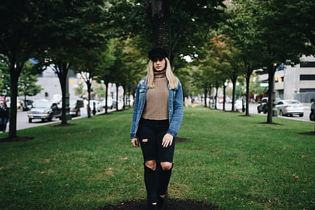 woman in brown shirt, blue jacket, and black pants standing on grass field thumbnail