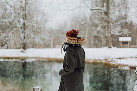person in black parka coat standing near body of water thumbnail