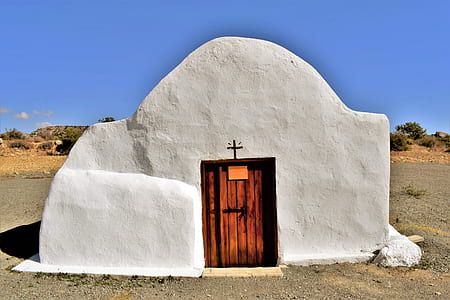 white concrete structure with brown wooden door surrounded by soil thumbnail